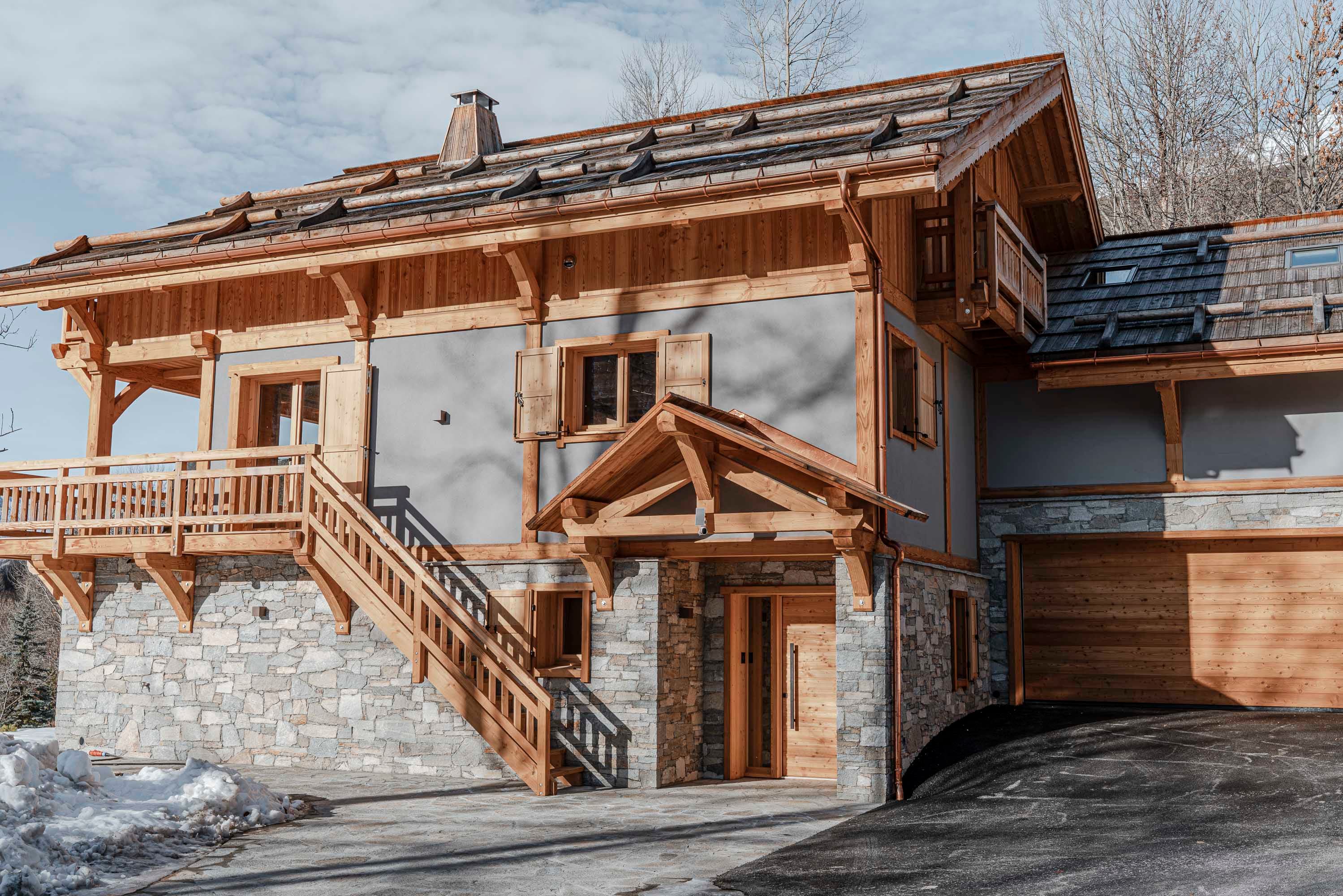 Entrée du chalet vue de face par temps ensoleillé, soubassement en pierre et auvent en bois