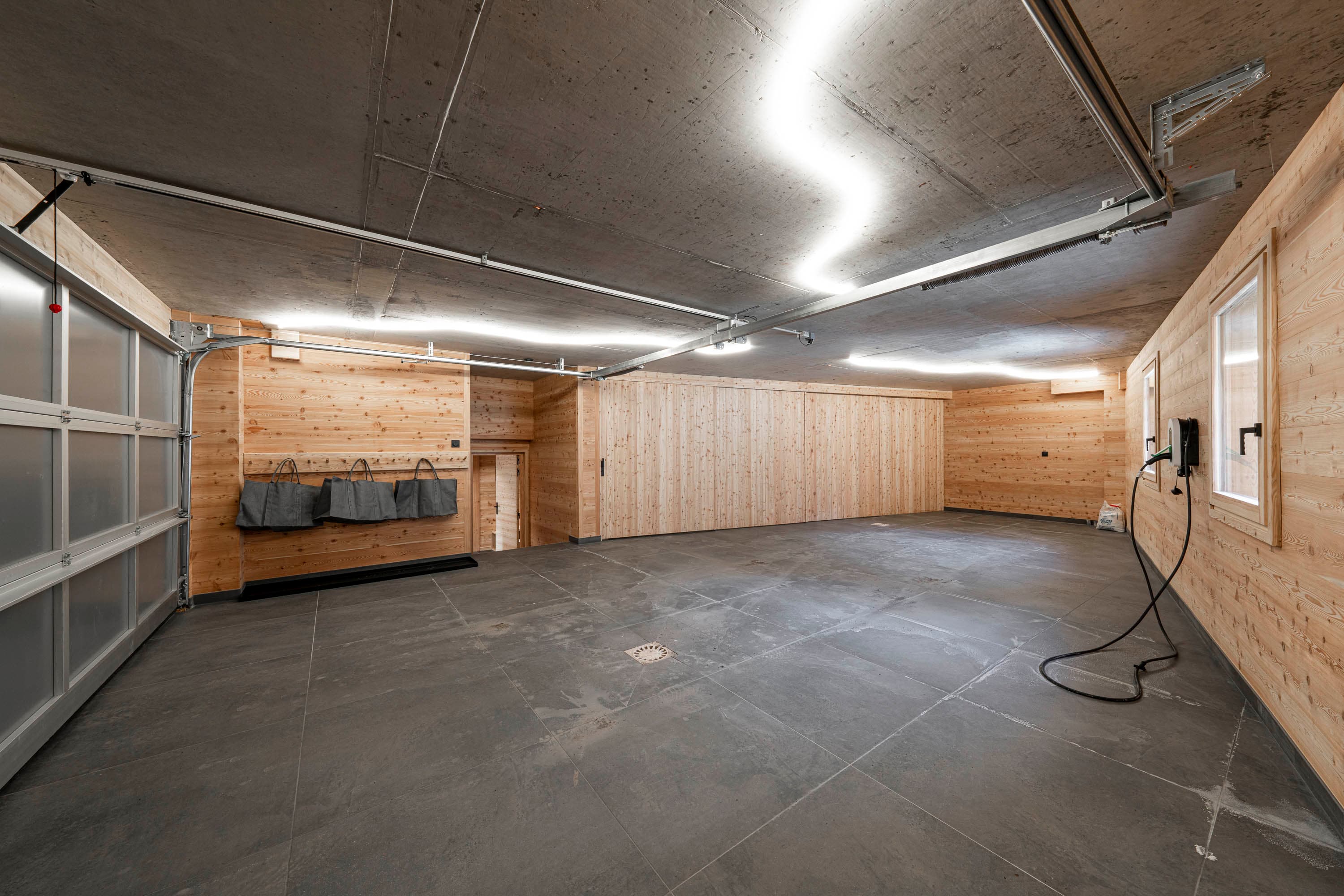 Grand garage avec porte sectionnelle, sol carrelé et borne de recharge électrique