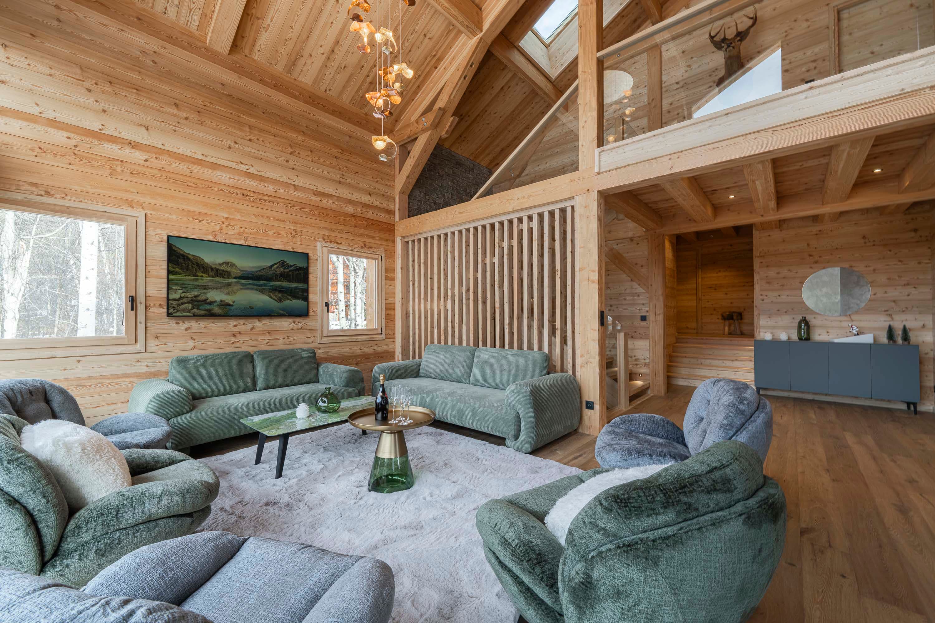 Vue plongeante du salon avec canapés, TV, tête de cerf à la mezzanine et suspension dorée