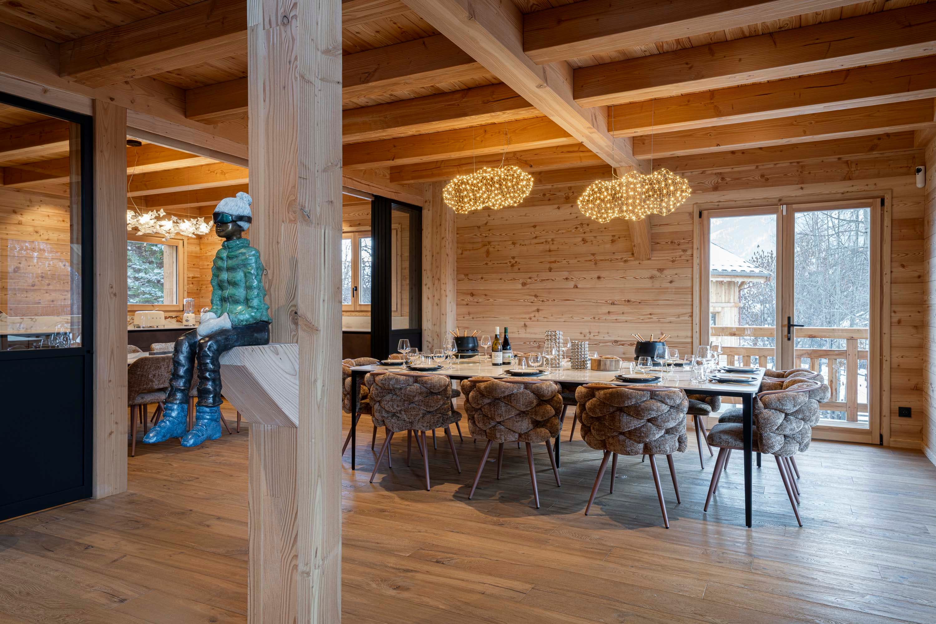 Salle à manger vue large avec sculpture de skieur, fauteuils tressés et suspensions nuage
