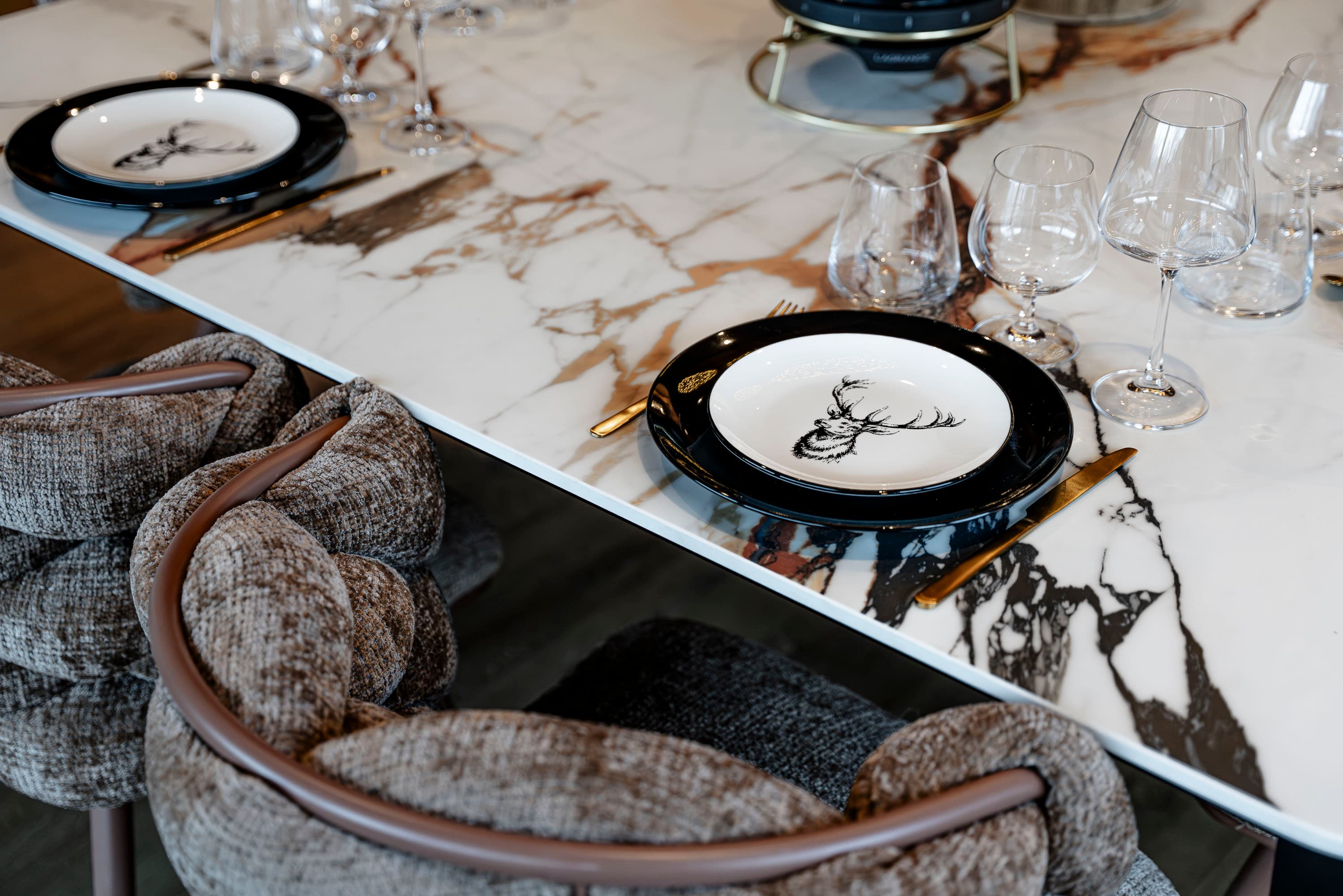 Détail de la table : assiettes au motif cerf, couverts dorés et plateau en marbre veiné