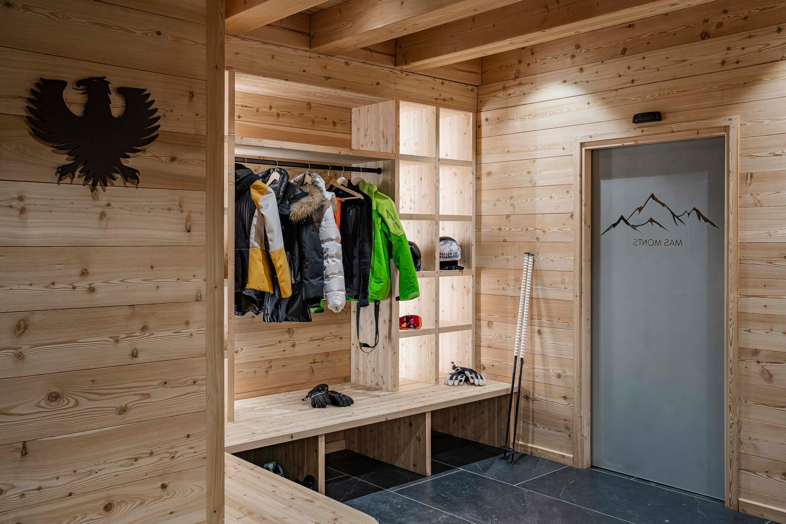 Vestiaire du ski room avec blason aigle, manteaux et porte vitrée Mas Monts