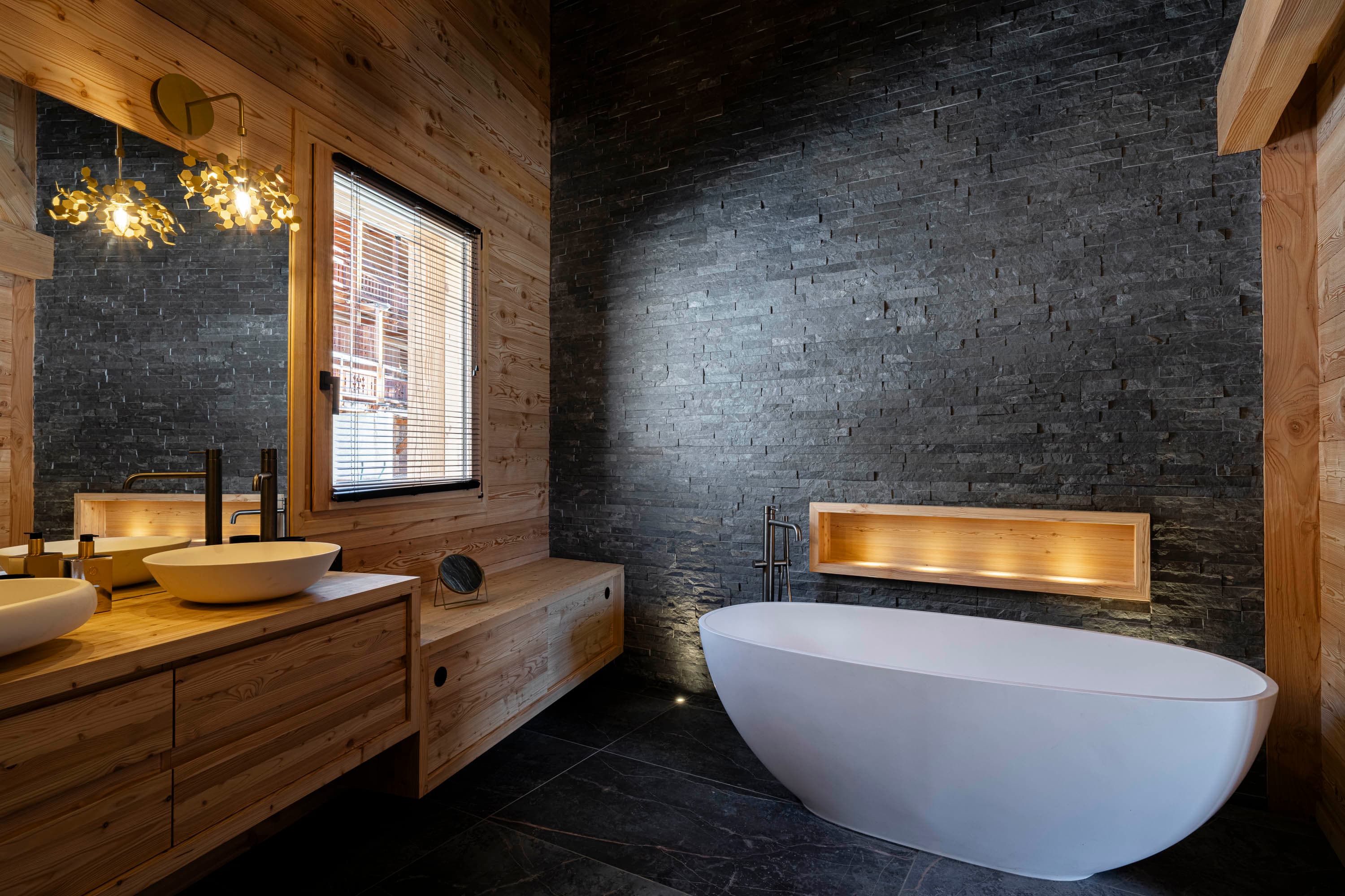 Baignoire îlot blanche devant un mur en ardoise noire avec niche en bois éclairée