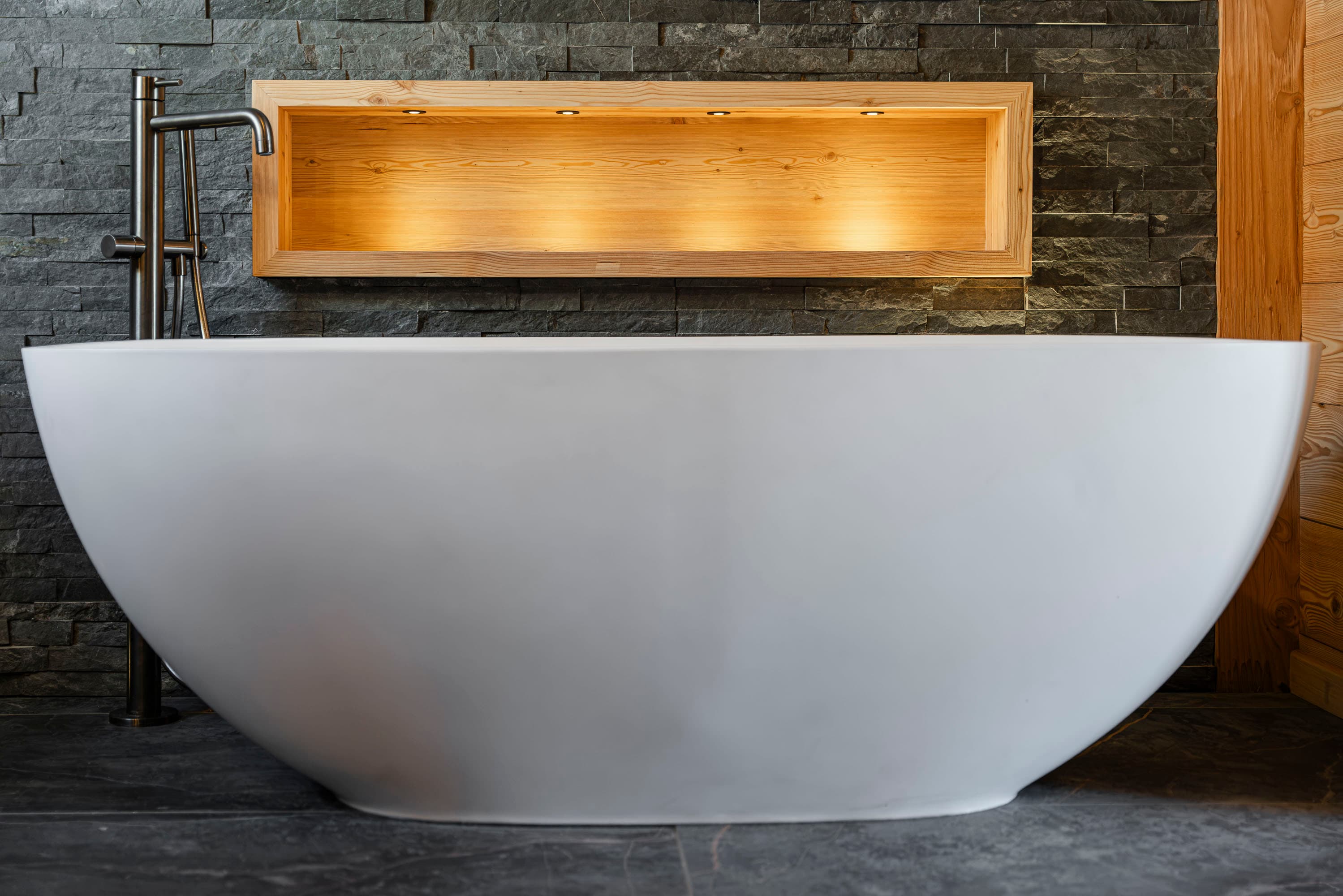 Gros plan de la baignoire îlot blanche avec robinetterie sur pied et niche éclairée